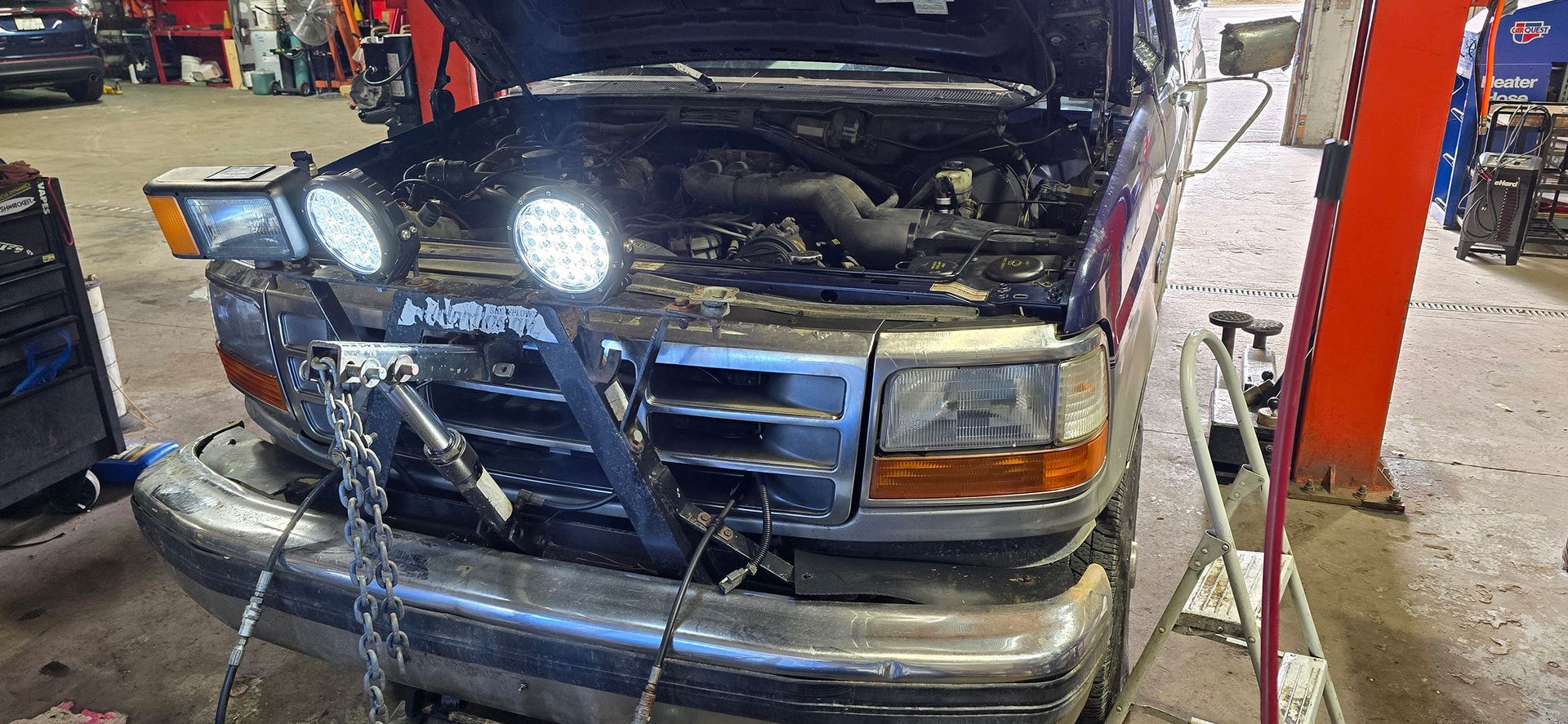 A truck with its hood up in a garage with engine lights attached to it.