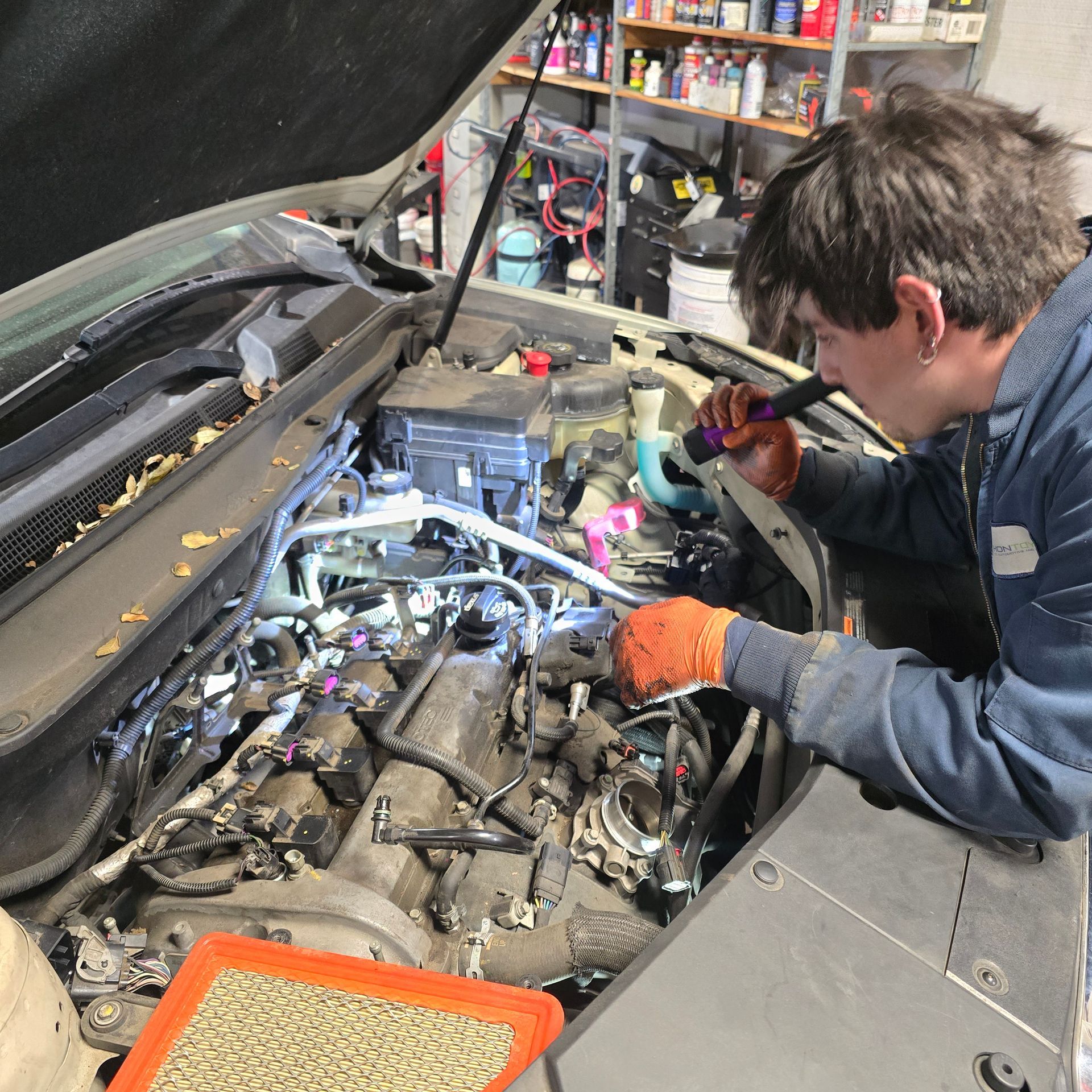 Person in work gloves examines car engine with a flashlight in a garage.