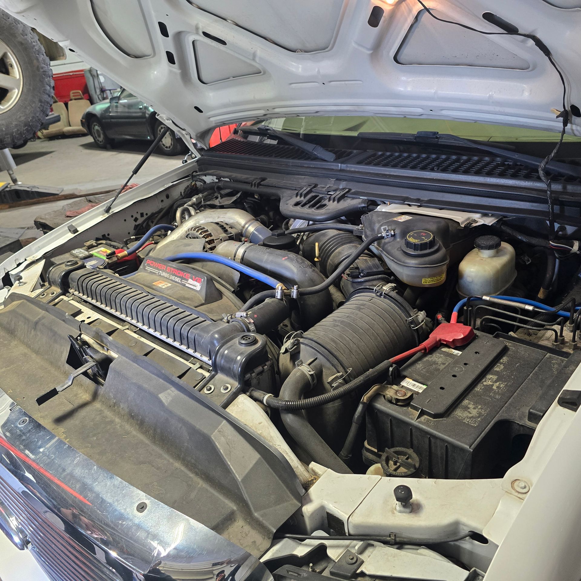 Open hood of a white truck, revealing the engine. Engine components are visible, including the battery and air intake.