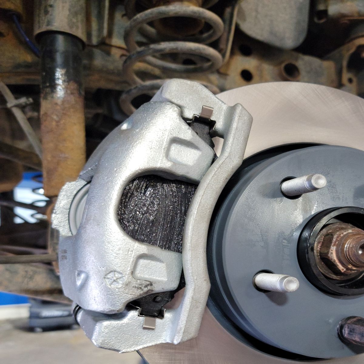 Car brake assembly with silver caliper, rotor, and suspension components.