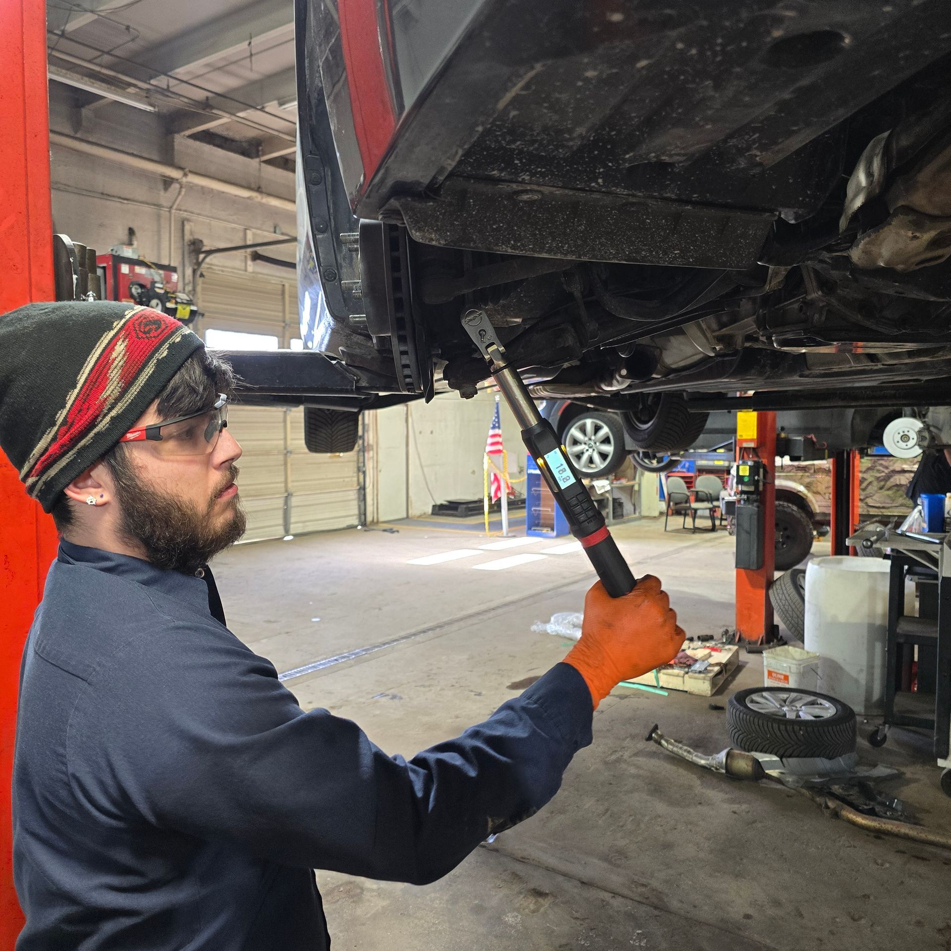 Mechanic working under a car, using a tool. Shop interior with car lift.