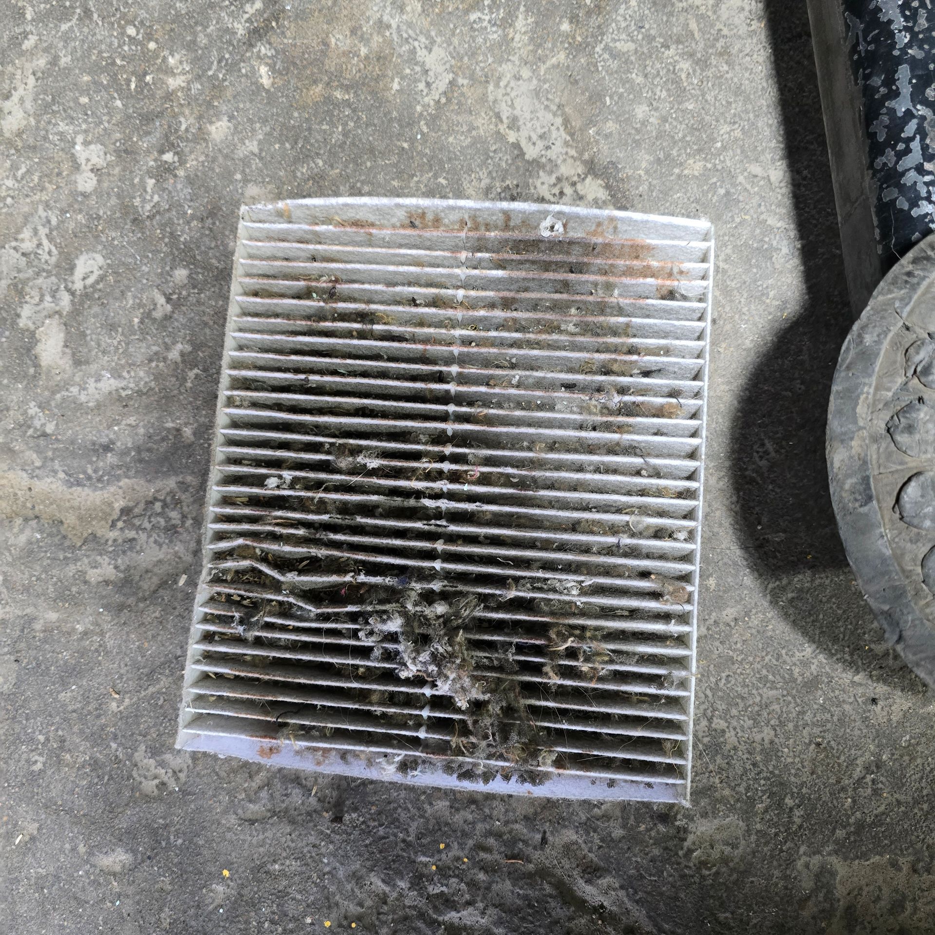 Dirty rectangular air filter on concrete surface, likely from a vehicle.