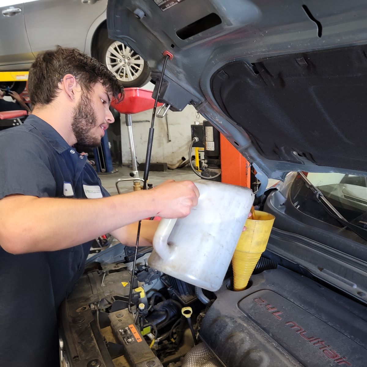 Mechanic pouring oil into a car engine, using a funnel. Auto shop setting.