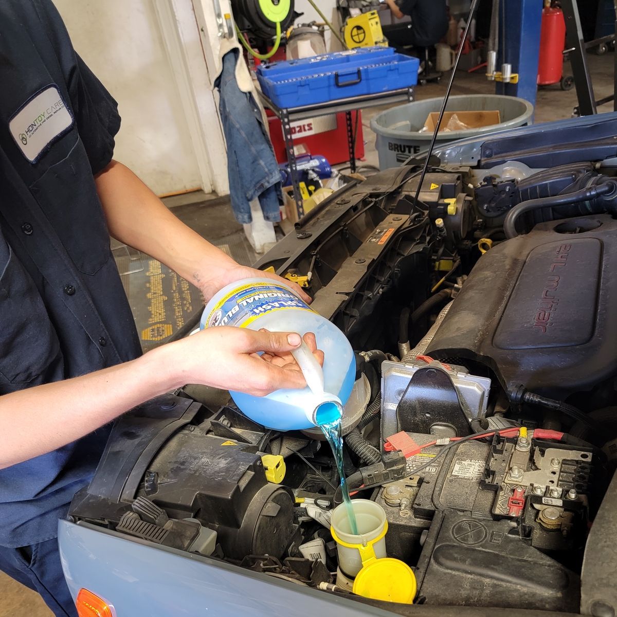 Person pouring blue windshield washer fluid into a car's reservoir in a garage.