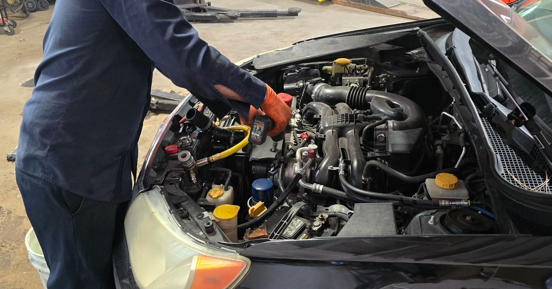 Person working on a car engine, wearing gloves and reaching inside. Hood open, daylight setting.