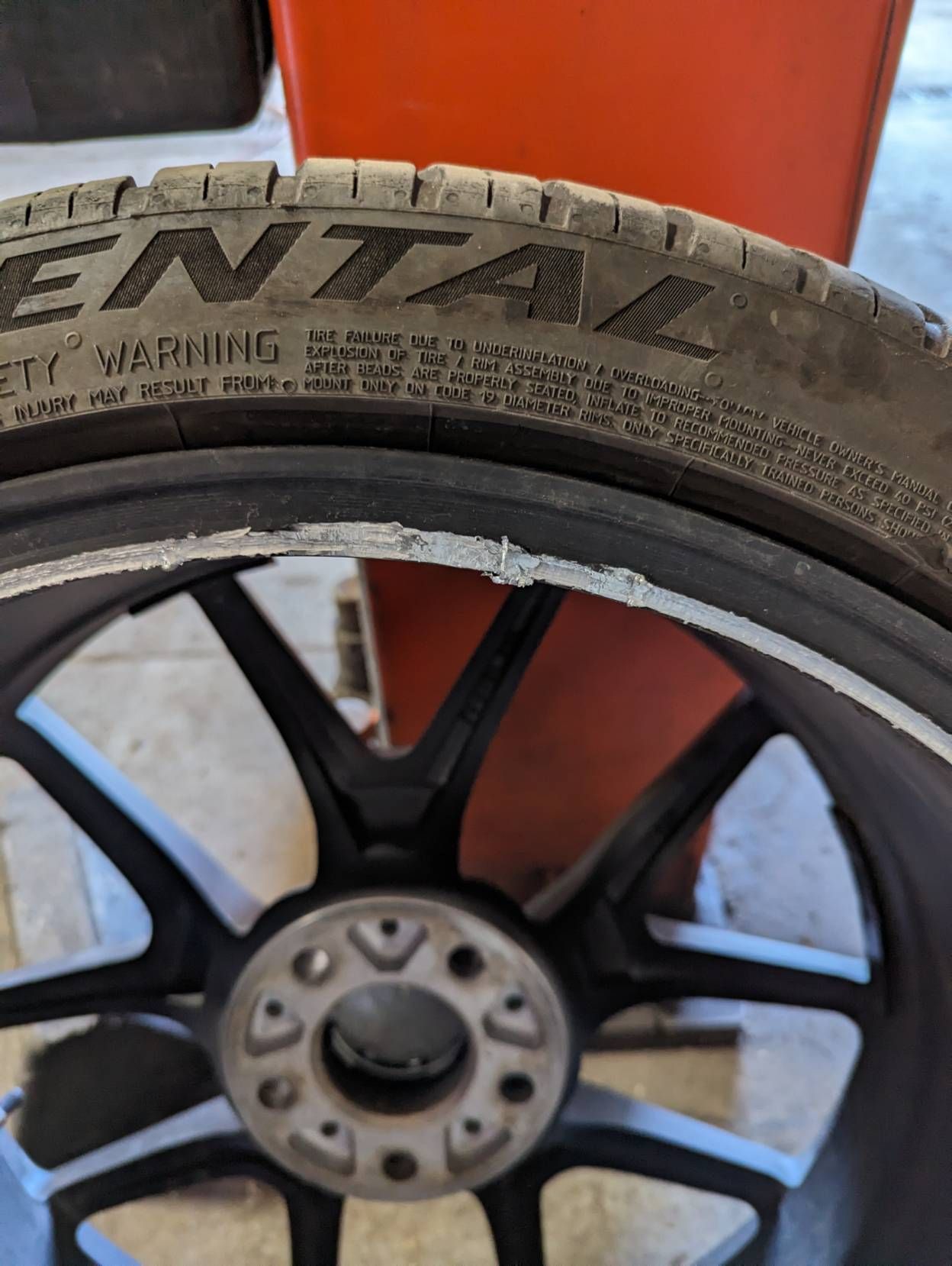 Close-up of a damaged black alloy wheel with a Continental tire. The wheel's rim has chipped paint.