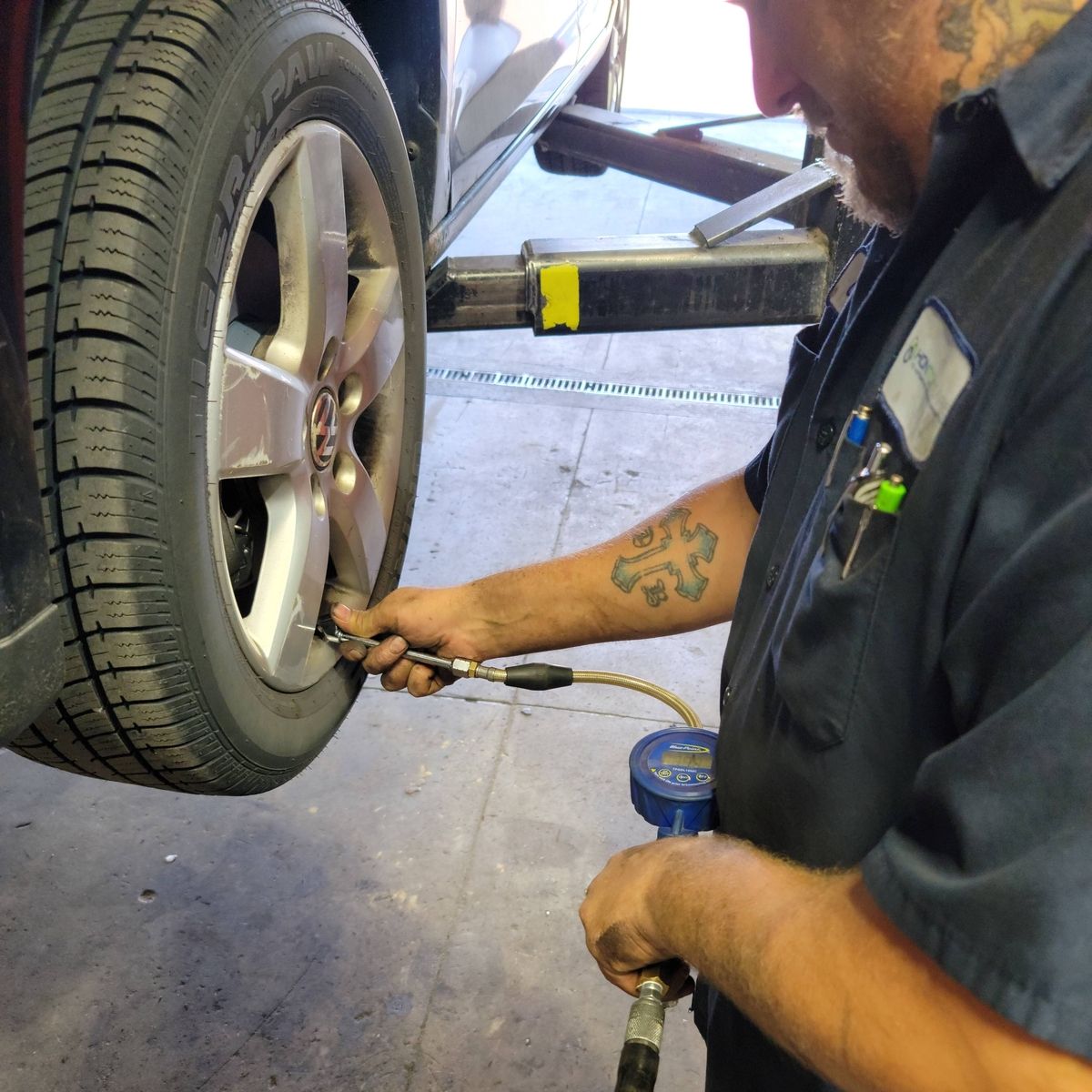 Mechanic inflates tire on a car lift; holding gauge. Automotive shop interior.