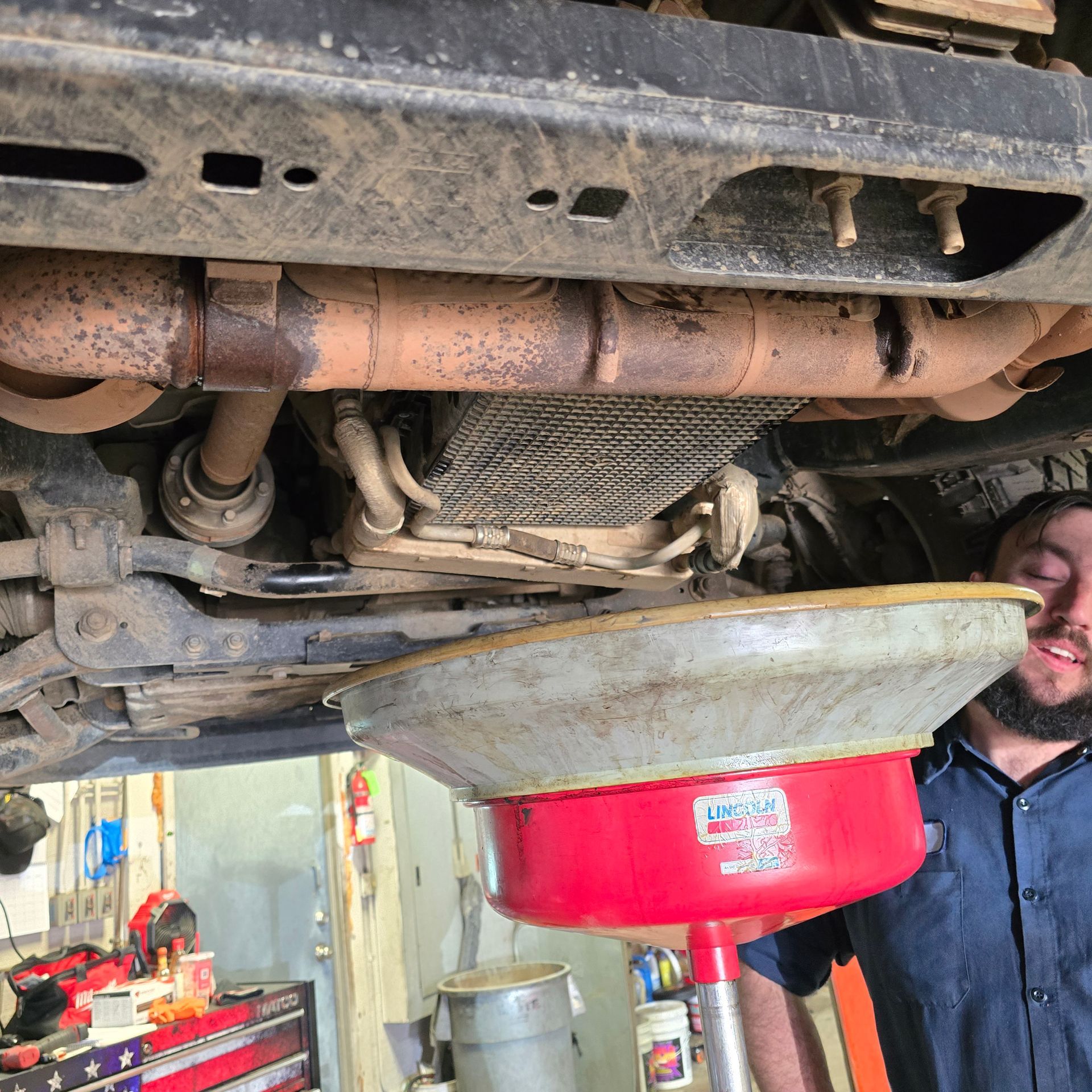 Man under a vehicle, draining oil into a pan in a garage.