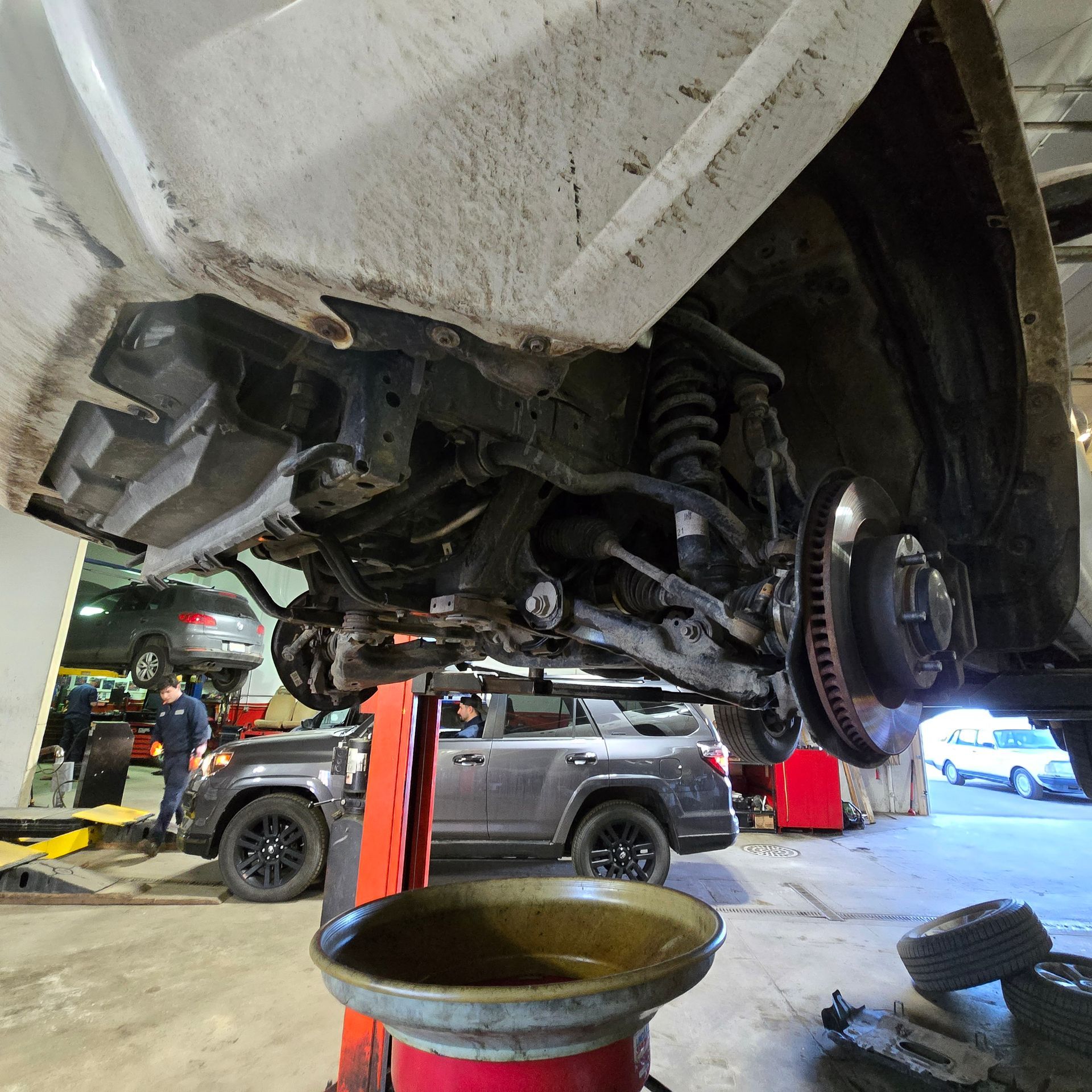 Underside of a vehicle on a lift in a repair shop, with exposed suspension components.