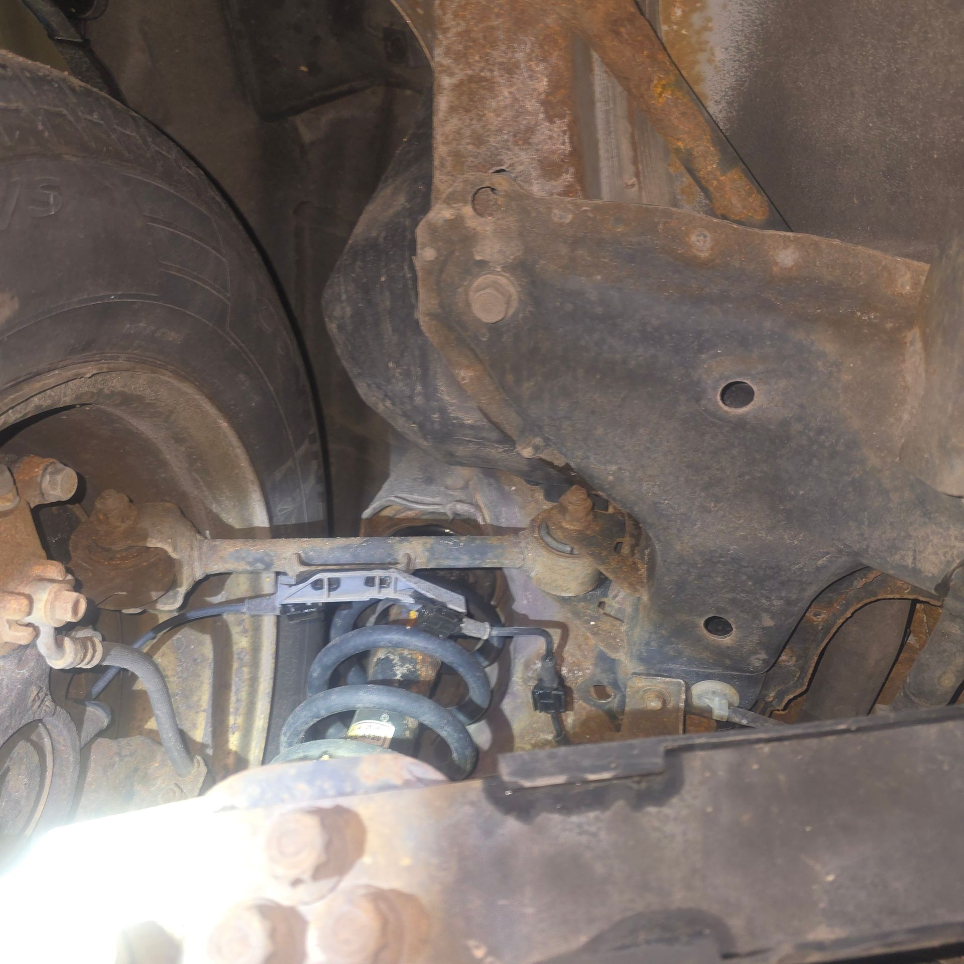 Underside of a vehicle, showing suspension components, including a coil spring and rusted metal frame.