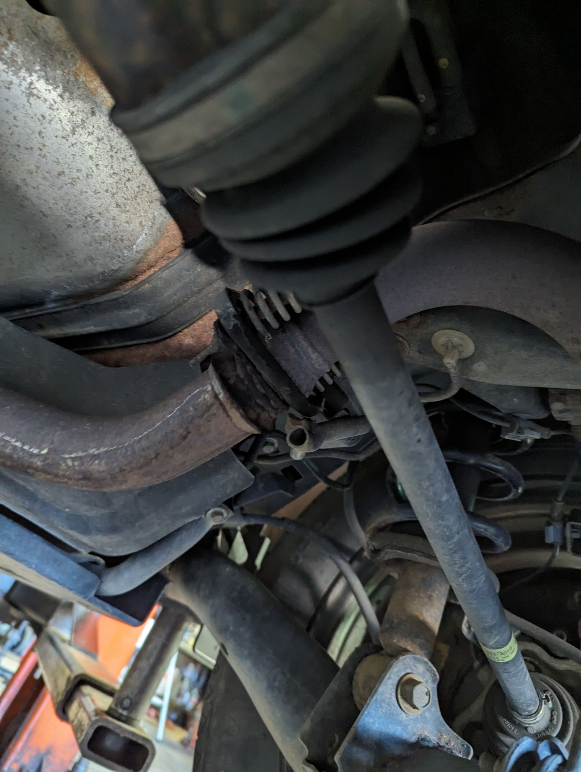 Undercarriage of a vehicle, showing a rusty exhaust pipe and a damaged CV joint boot.