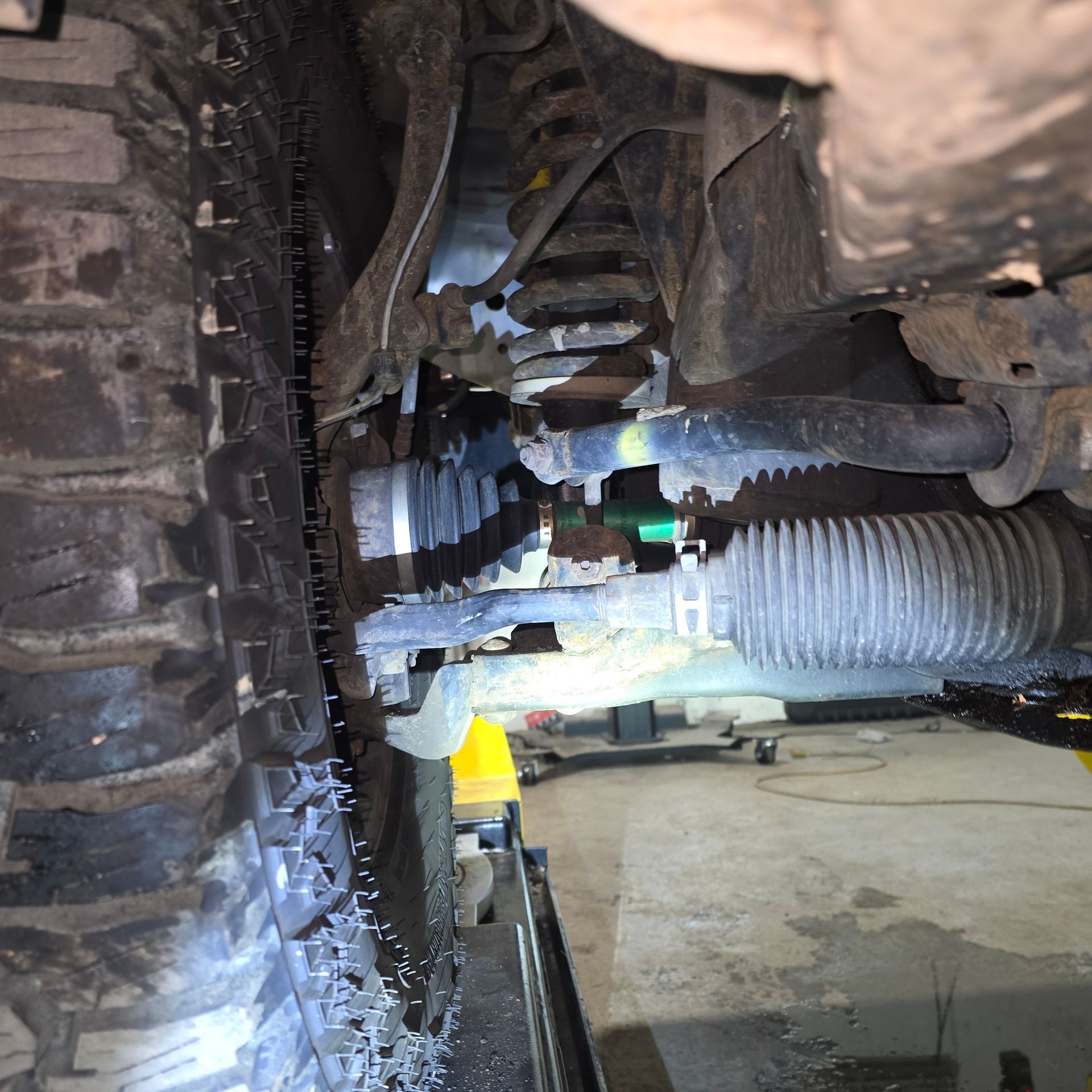 Underside of a vehicle showing suspension, tire with chains, and steering components in a garage.