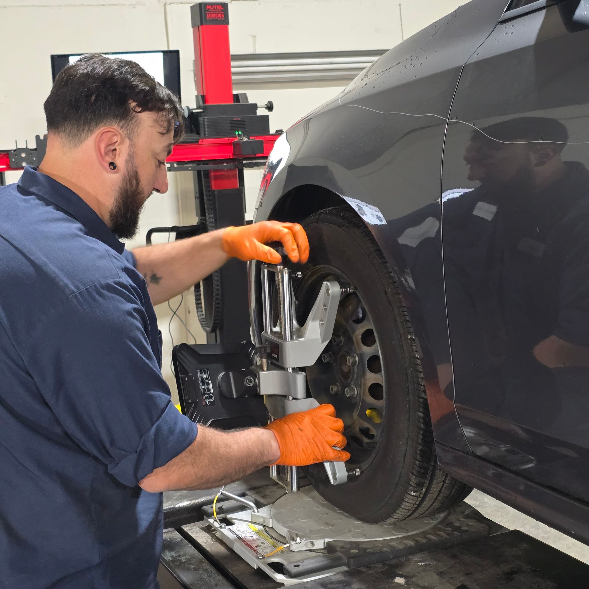 Mechanic adjusting alignment tool on a car's wheel in a shop.