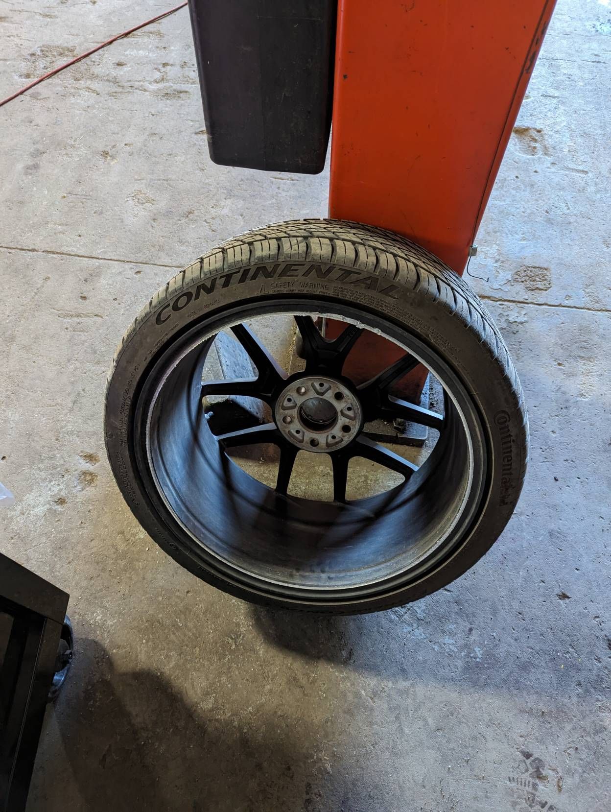 A tire and rim balanced on a red and black machine in a garage setting.