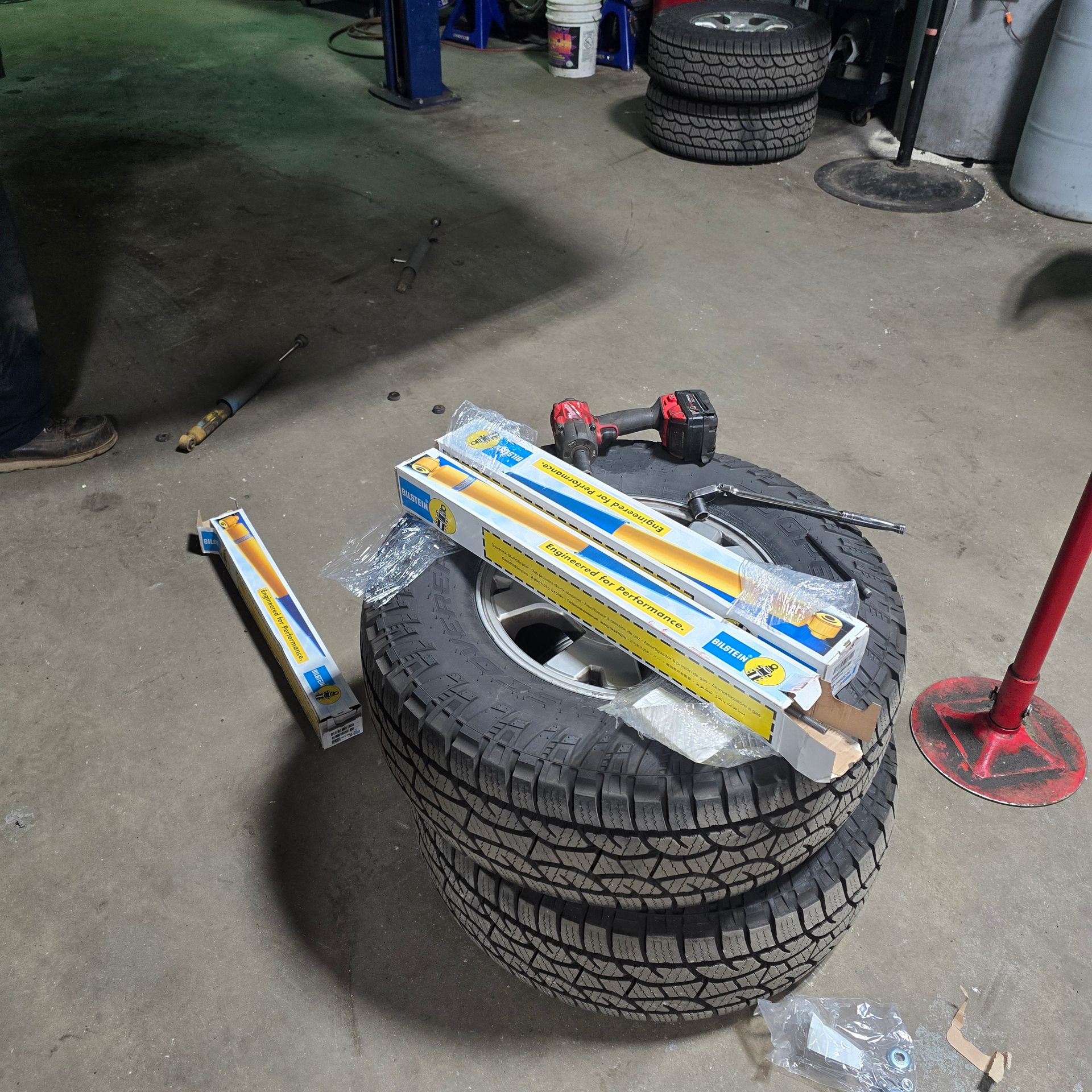 Two new shock absorbers and a cordless drill sit on a tire stack in a garage.