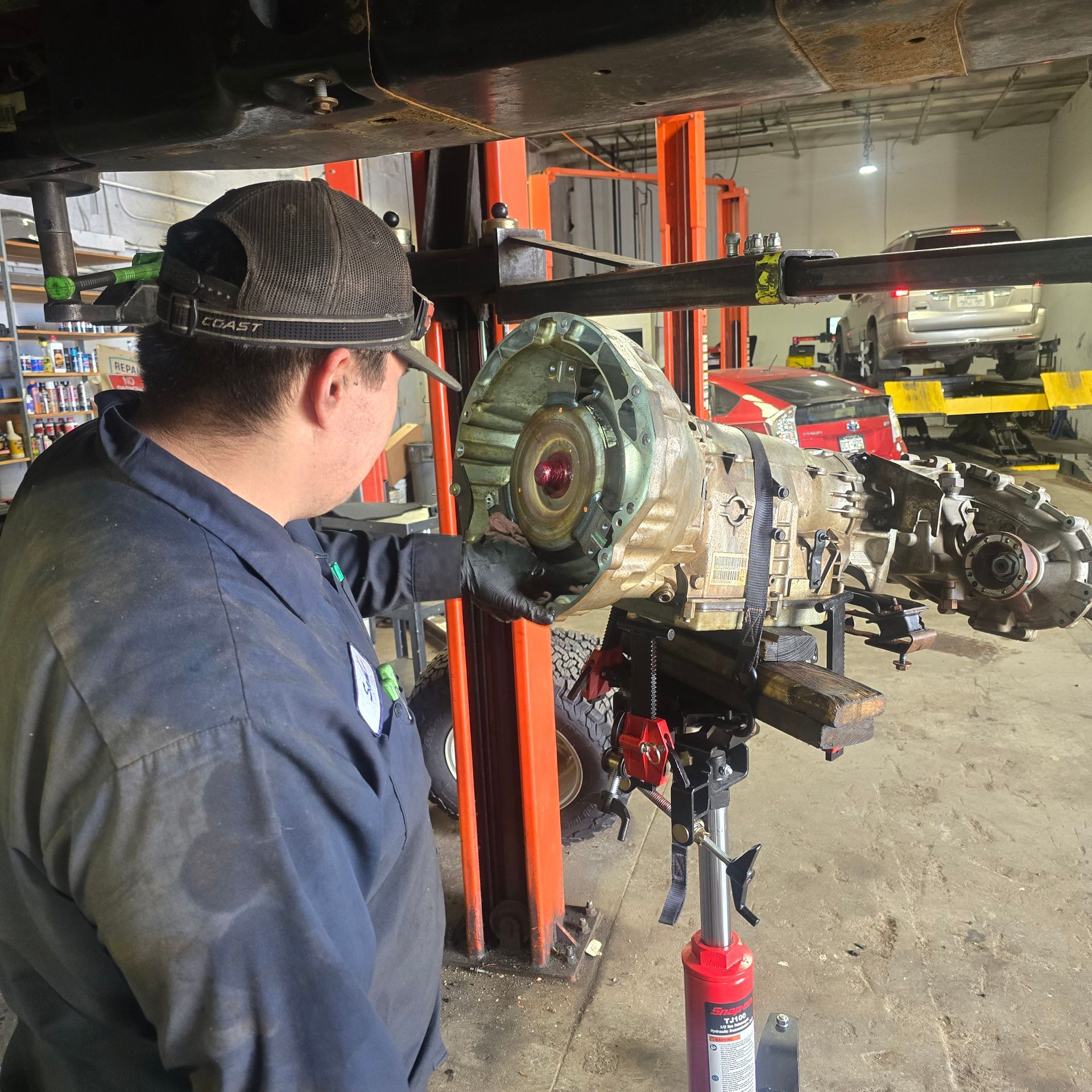 Mechanic working on car transmission in auto shop. He is focused, with tools on the table.