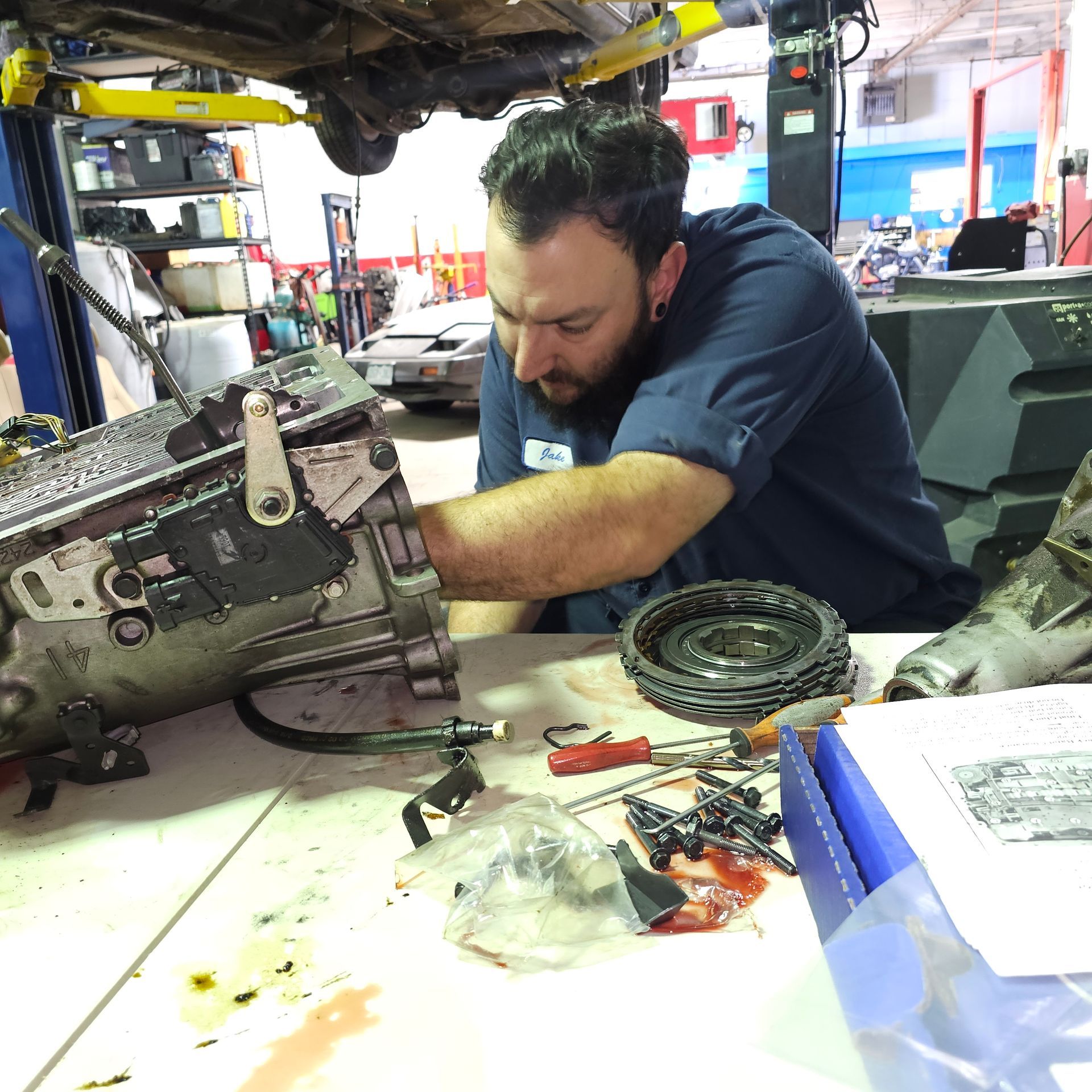 Mechanic working on car transmission in auto shop. He is looking down intently.