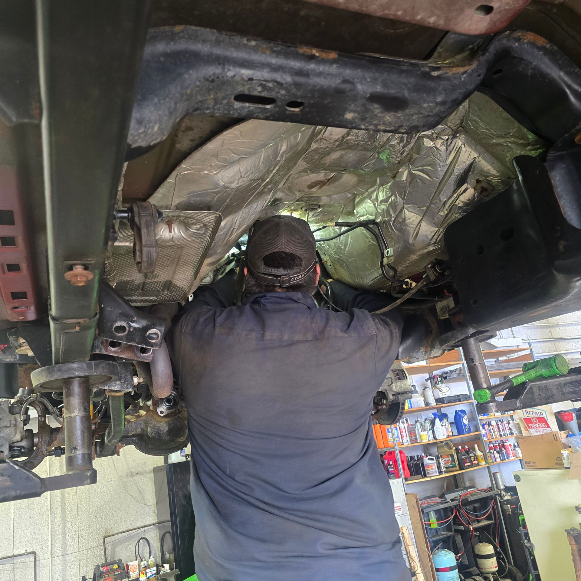 Mechanic working on the underside of a vehicle. Shop environment, using tools, with overhead view.