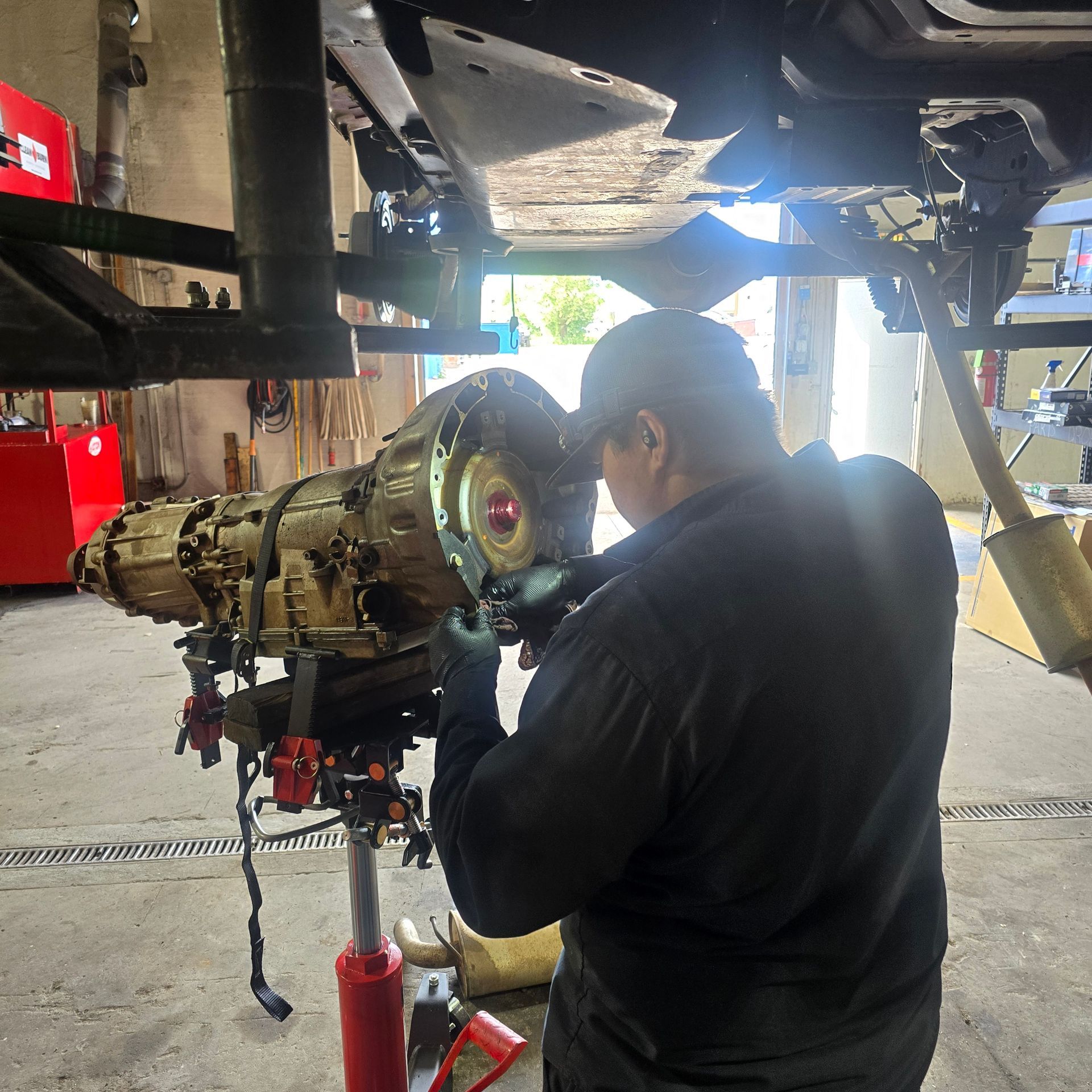 Mechanic working on a car's undercarriage in a garage; he is fixing the vehicle's transmission.