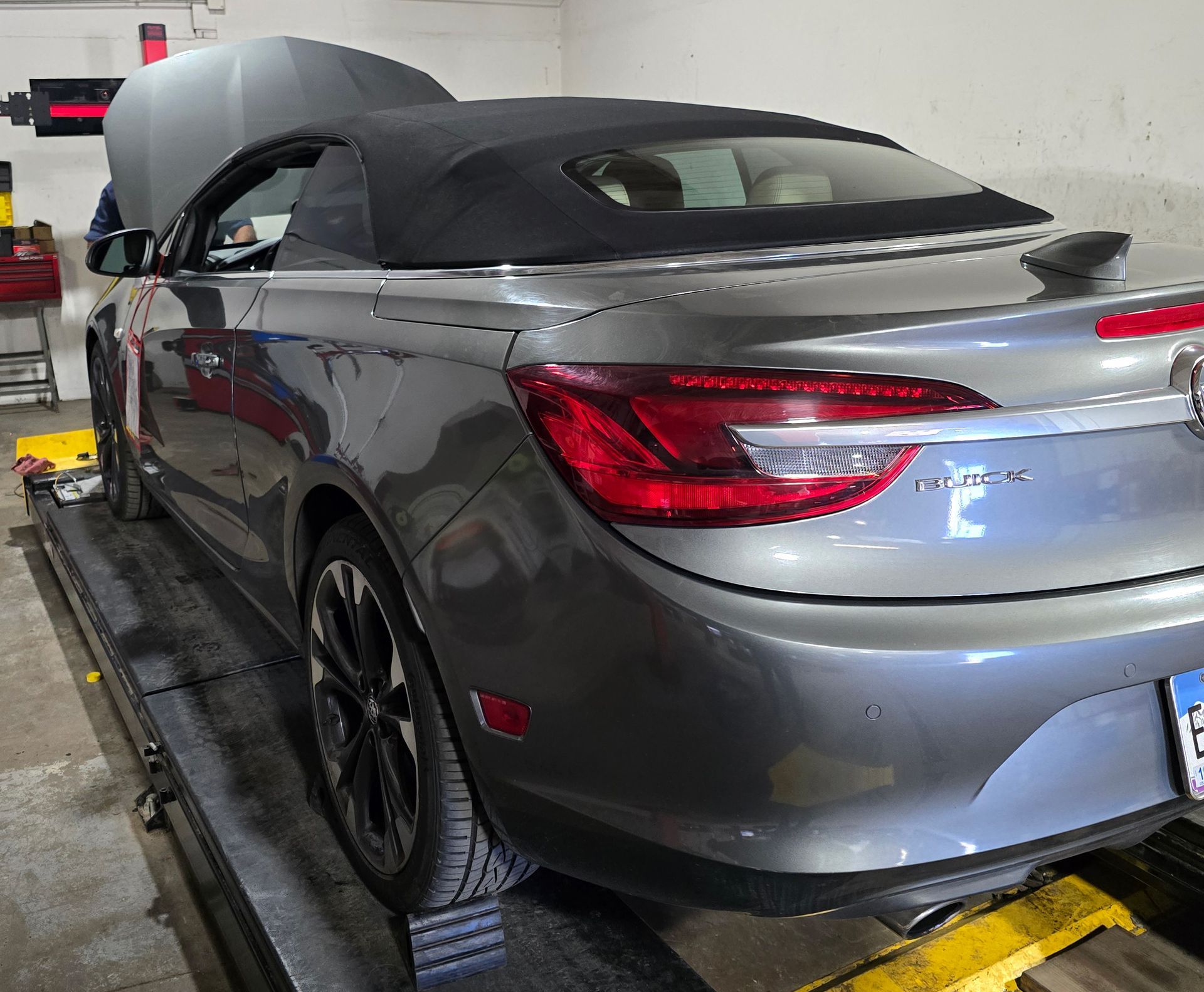 Gray Buick convertible with the hood up, parked in a garage.