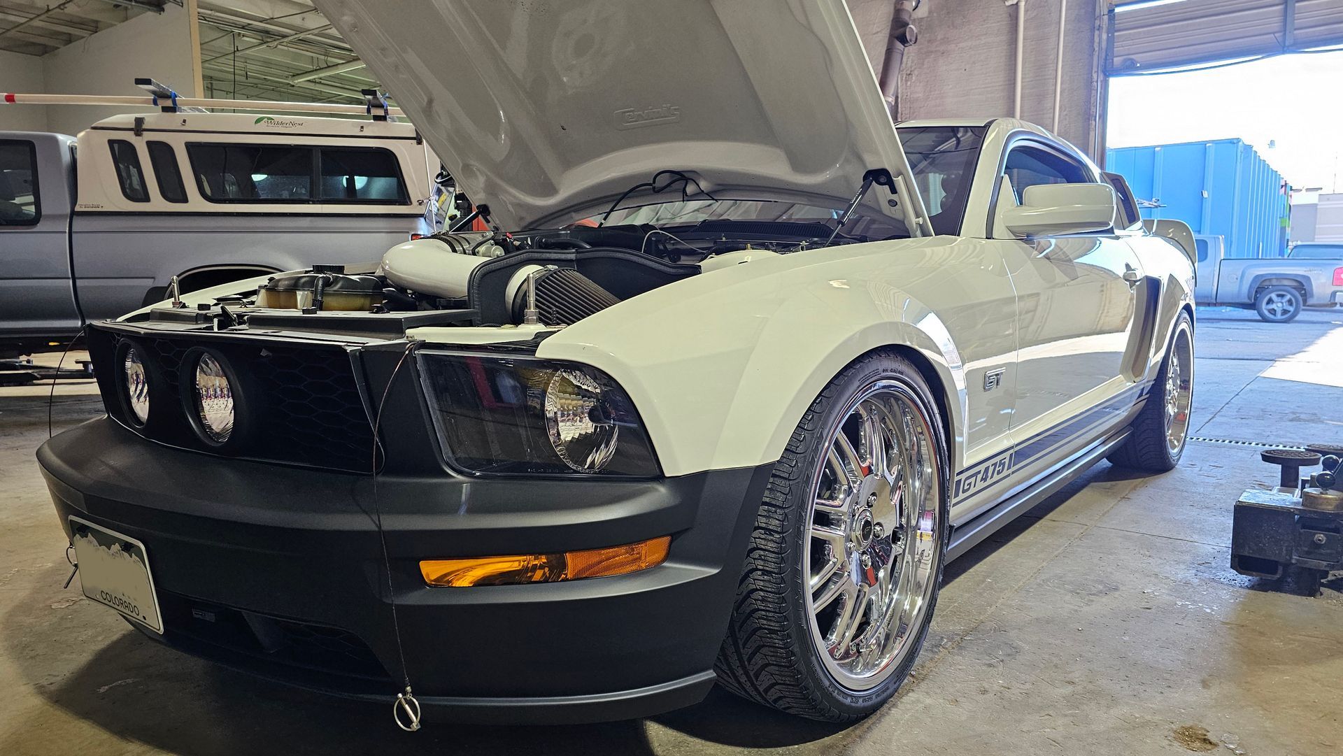White Ford Mustang with the hood open, parked in a garage.