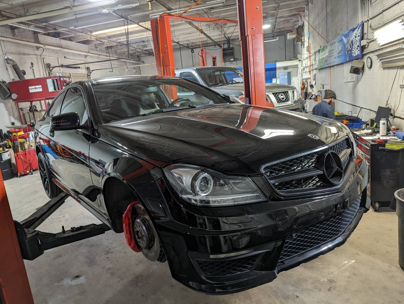 Black Mercedes-Benz C-Class sedan raised on a lift inside a garage. Front wheel removed, red brake calipers visible.