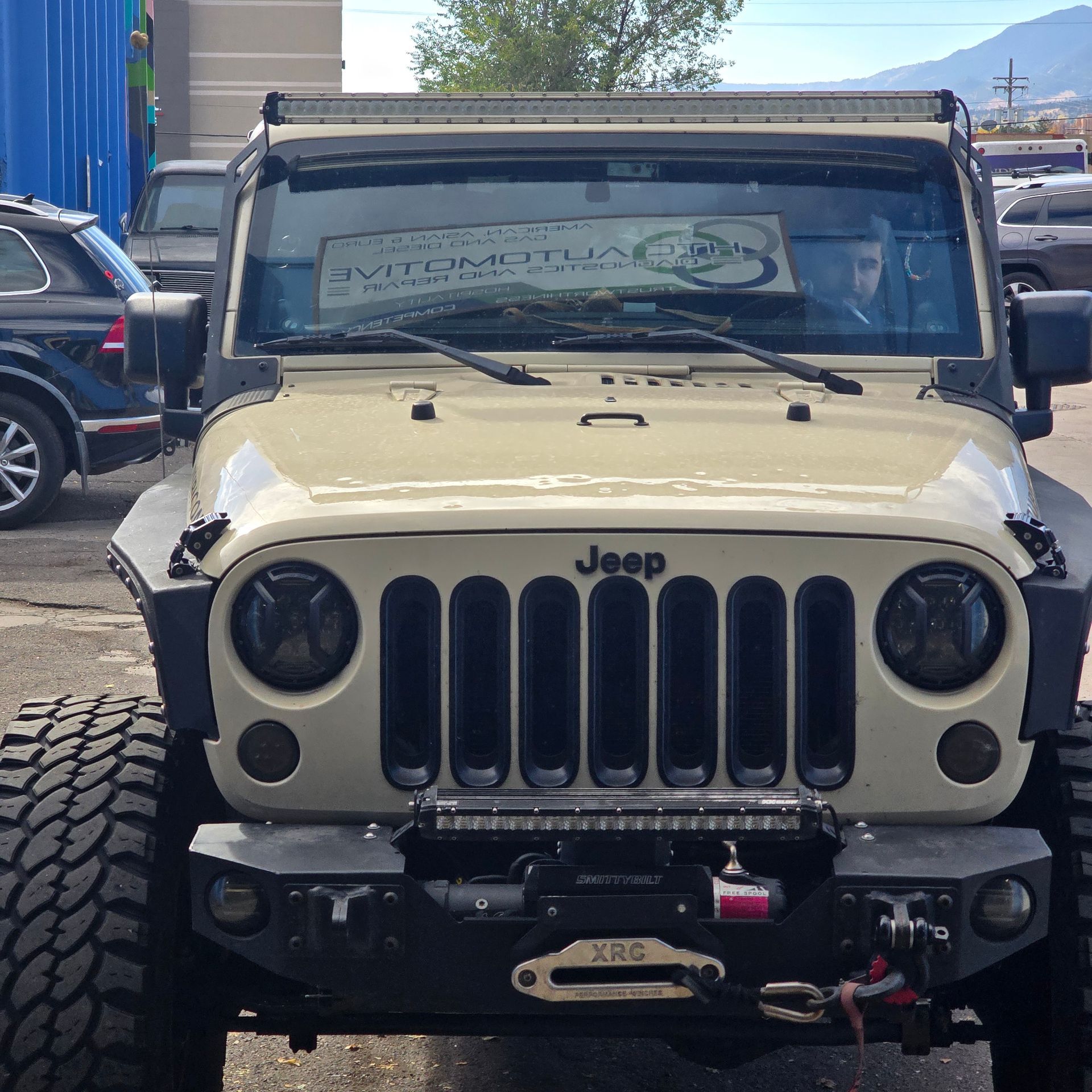 Tan Jeep Wrangler with black accents, light bars, and large tires.
