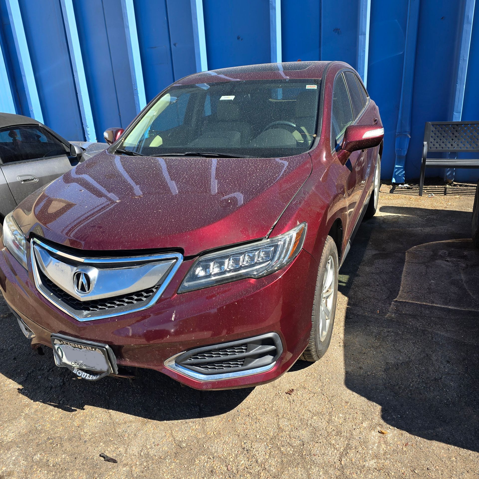 Red Acura RDX SUV parked outdoors near a blue wall and a bench.