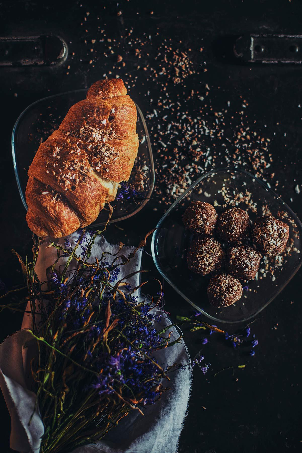 Croissant, truffles, and flowers arranged on a dark table with sprinkled seasoning