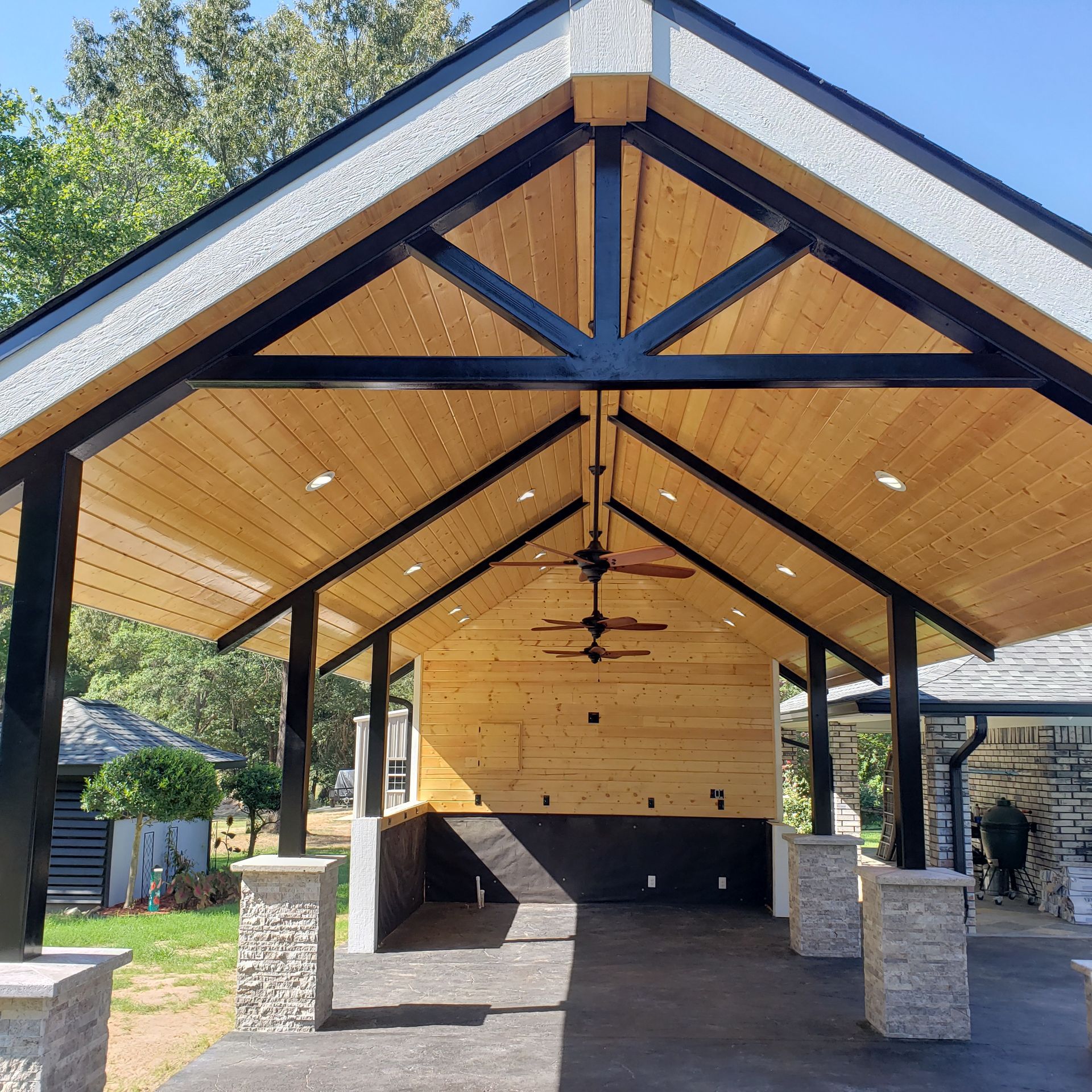 Open-air wooden patio with black beams, recessed lights, and stone columns.