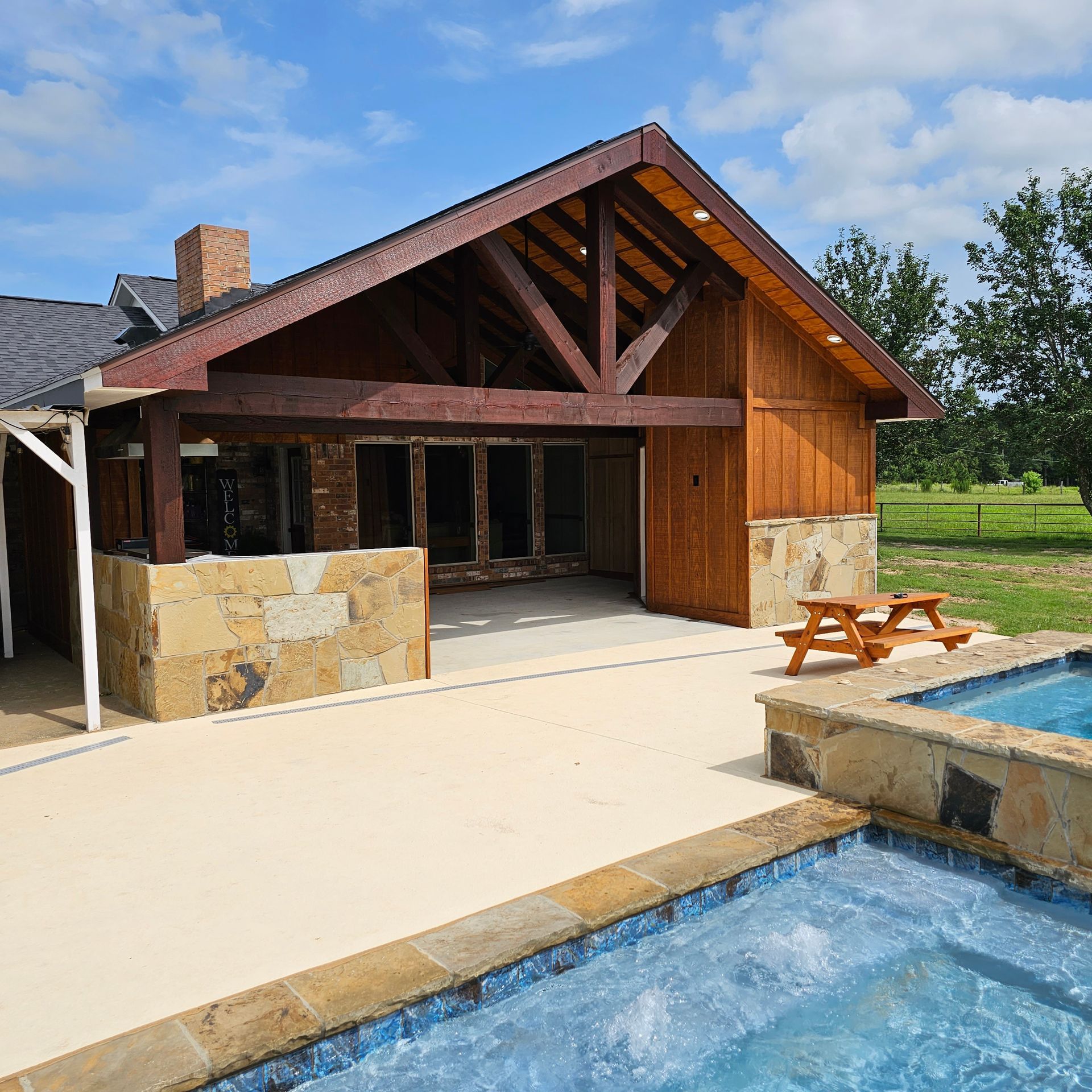 A wooden building with a pool, patio, and stone accents under a blue sky.