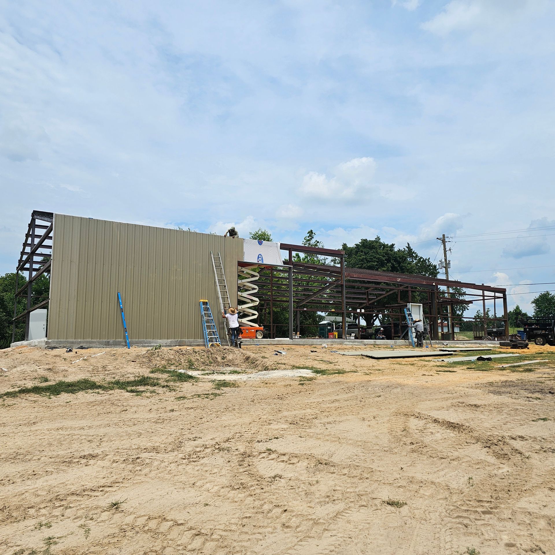 Construction site with metal framing and concrete walls under a cloudy sky.