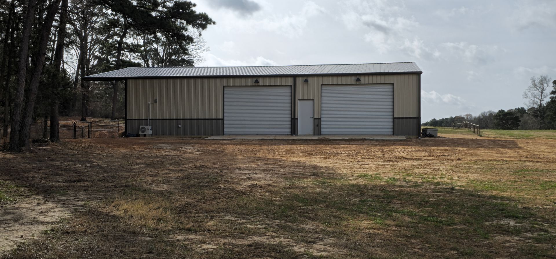 Garage with two bays in a grassy field, trees in the background, overcast sky.