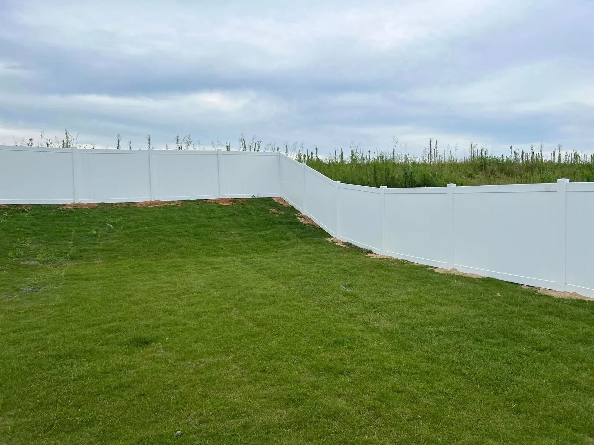 White vinyl fence encloses a grassy backyard on a cloudy day.