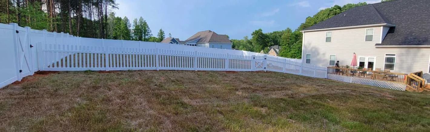 A white picket fence surrounds a grassy yard. A two-story house is on the right.