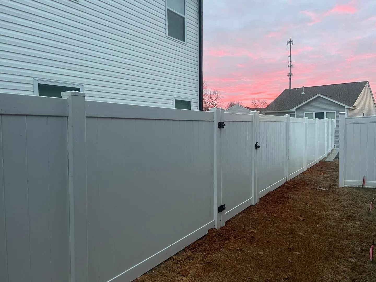 White privacy fence extending toward a house with a pink and blue sunset.