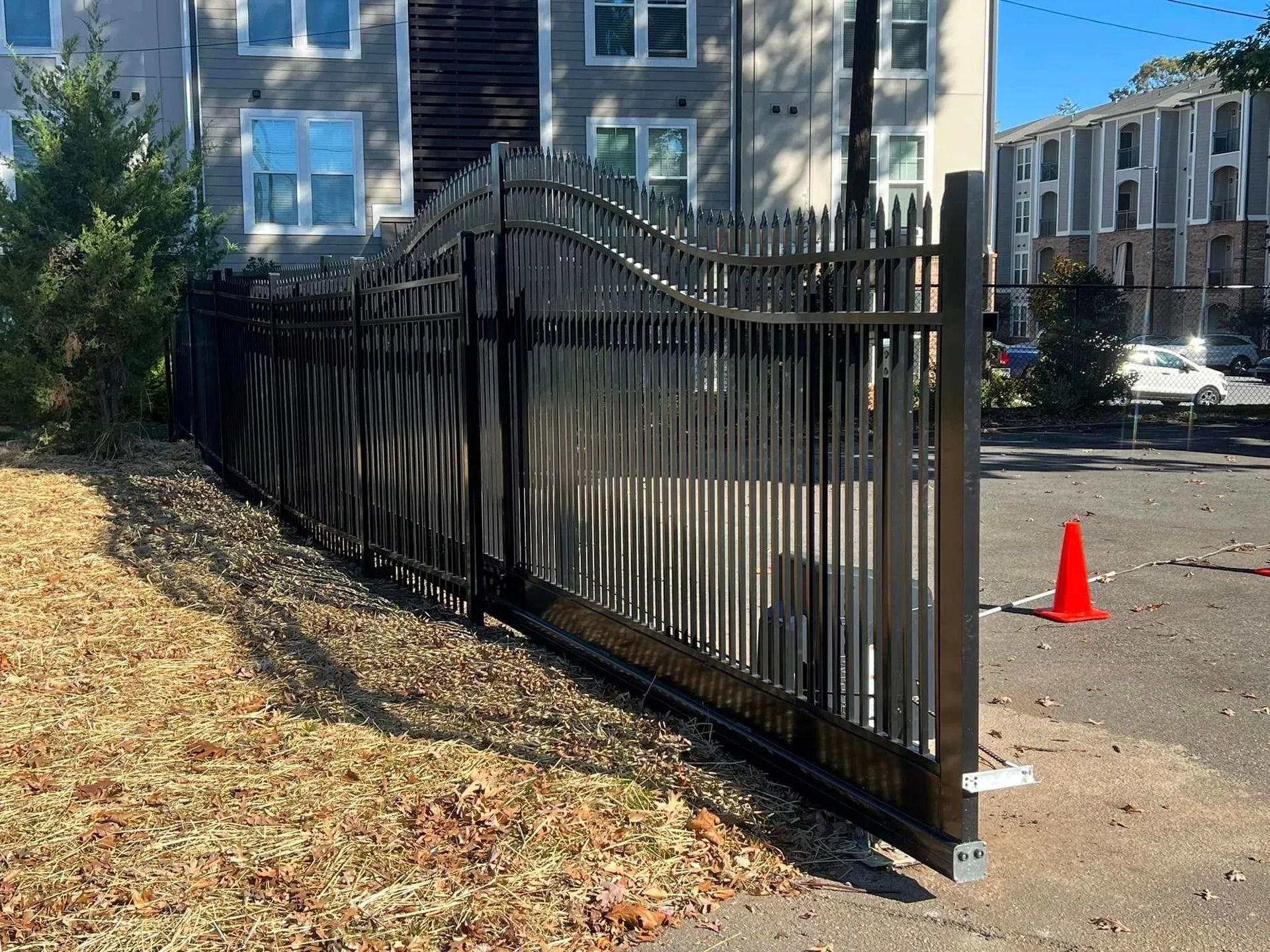 Black metal security gate along a building, next to a sidewalk and grassy area.
