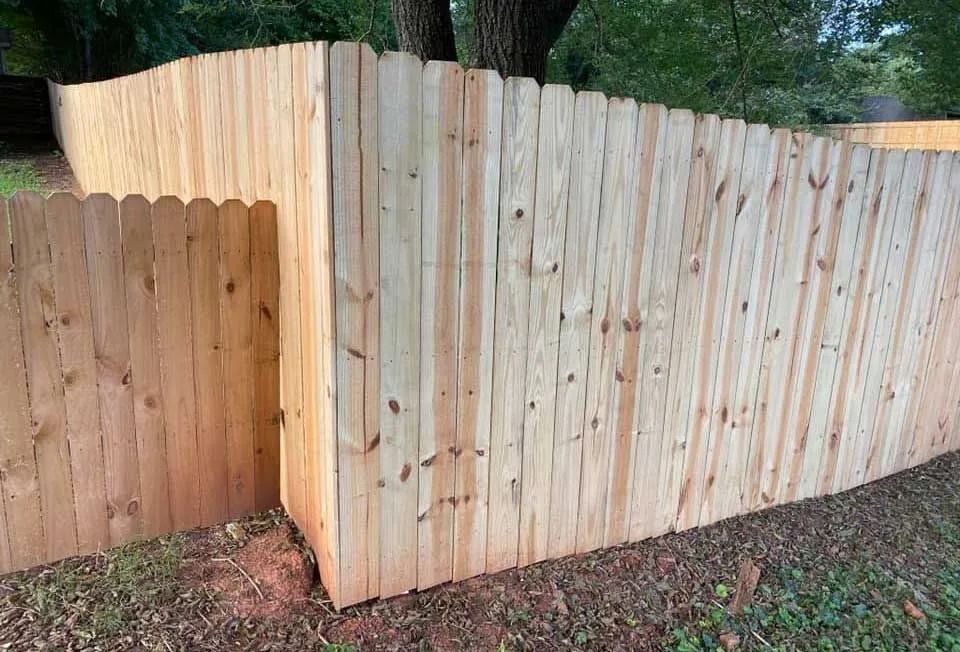 Wooden privacy fence enclosing a yard, with scalloped top boards.