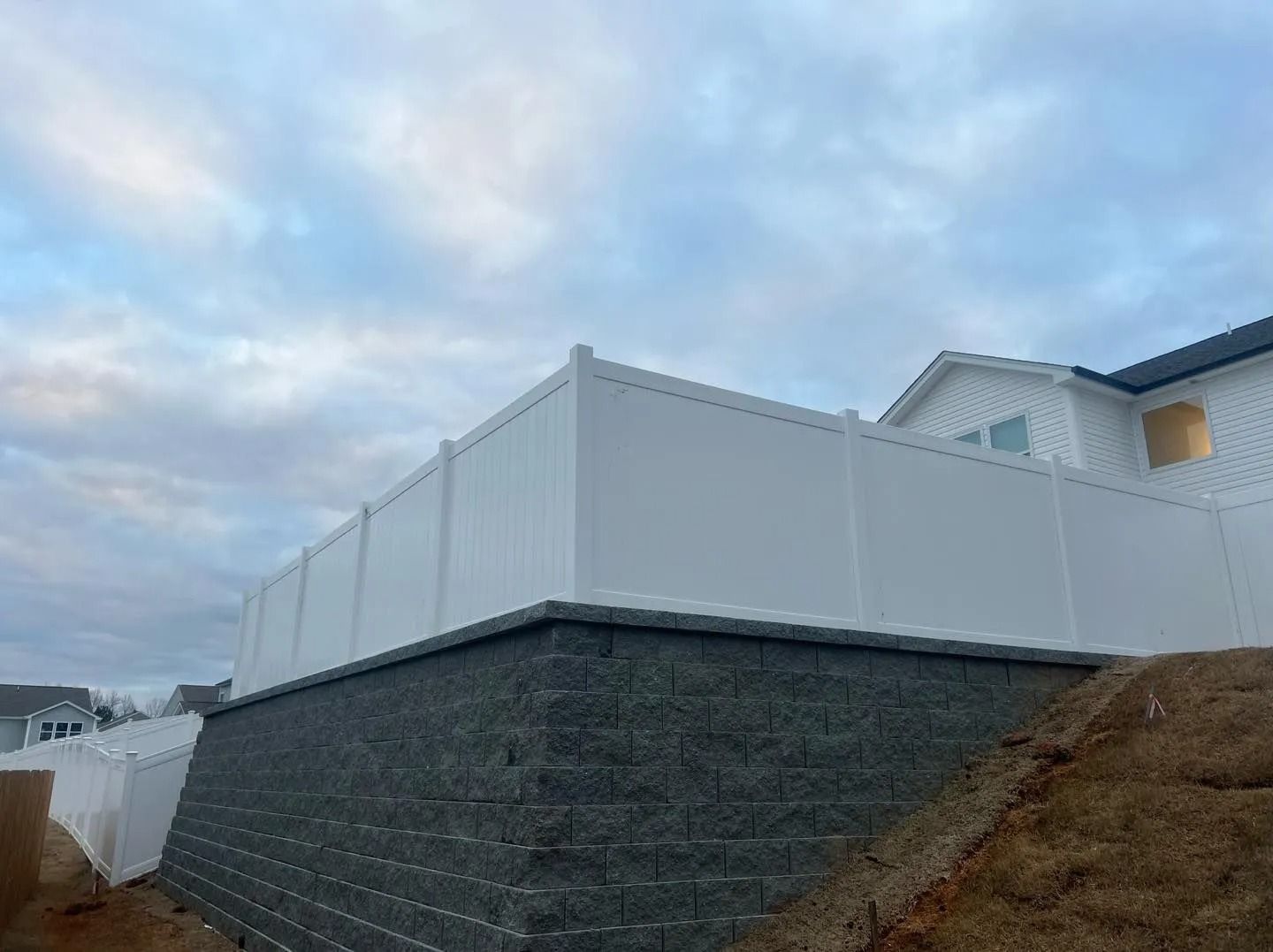 White vinyl fence atop a retaining wall, under a cloudy sky.
