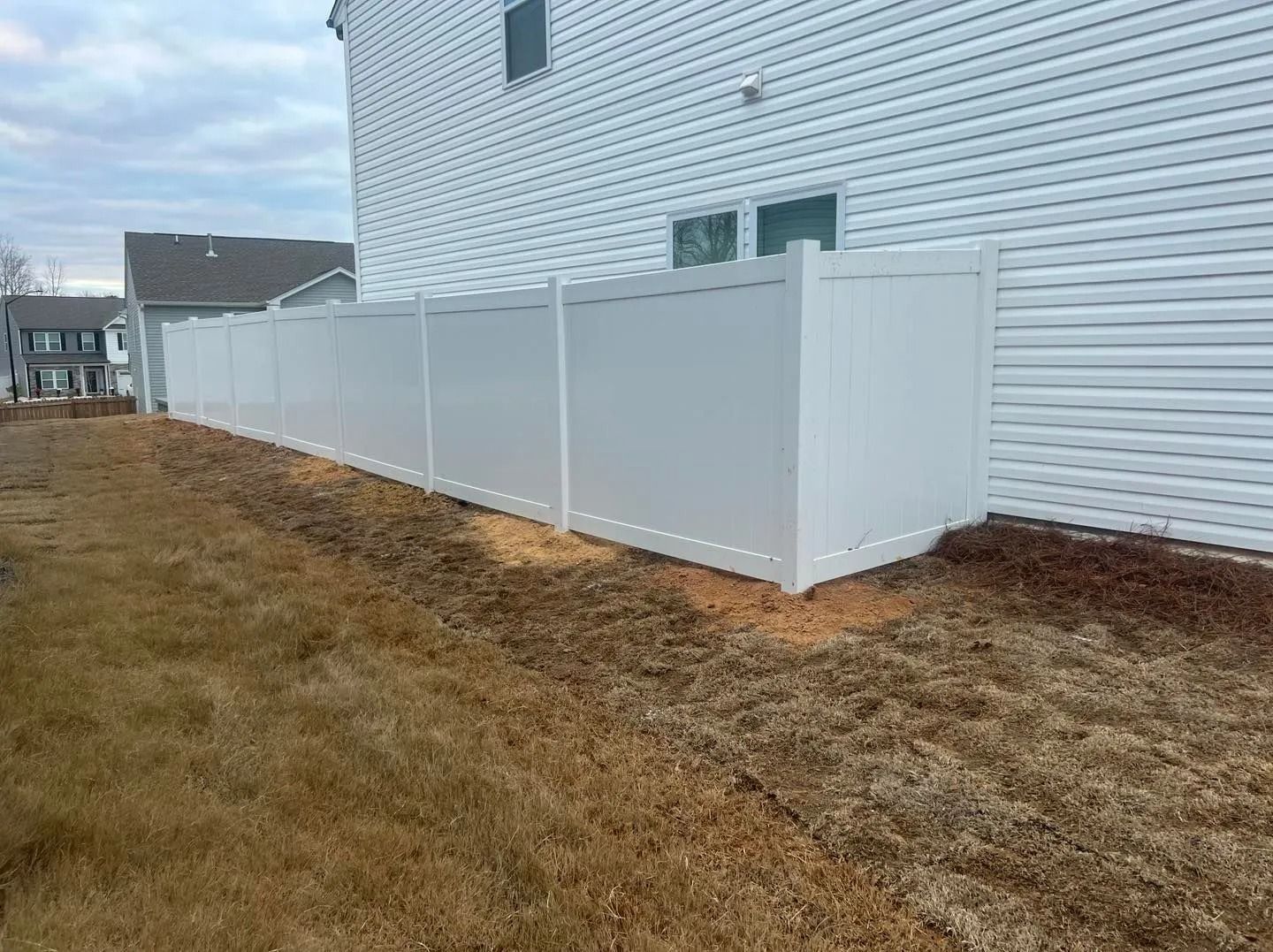 White vinyl fence along the side of a house, set in a yard with brown grass.