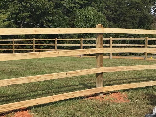 Wooden split-rail fence in a grassy yard, with trees in the background.