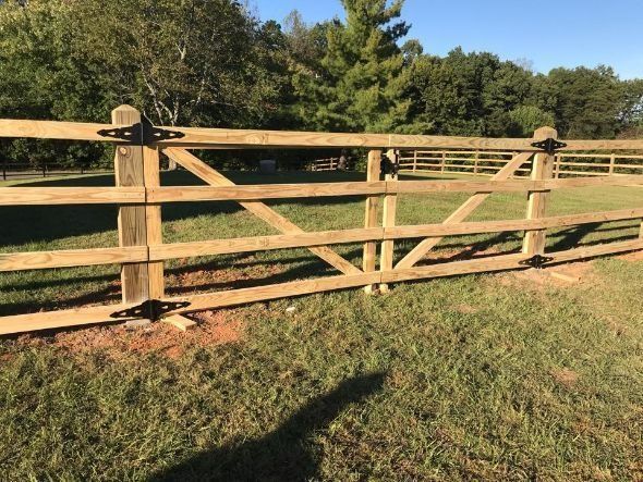 Wooden gate in a grassy field, attached to a wooden fence.