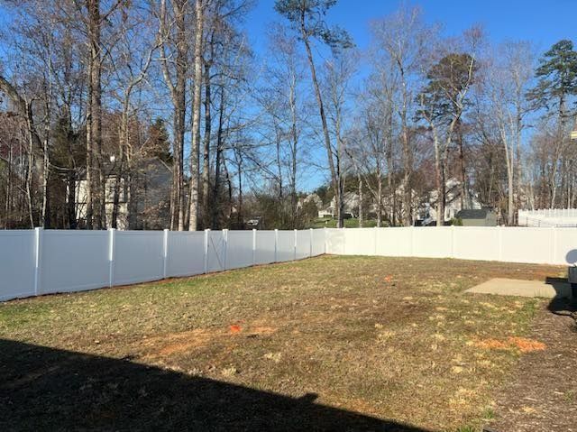 White vinyl fence encloses a grassy backyard with bare trees and a bright blue sky.