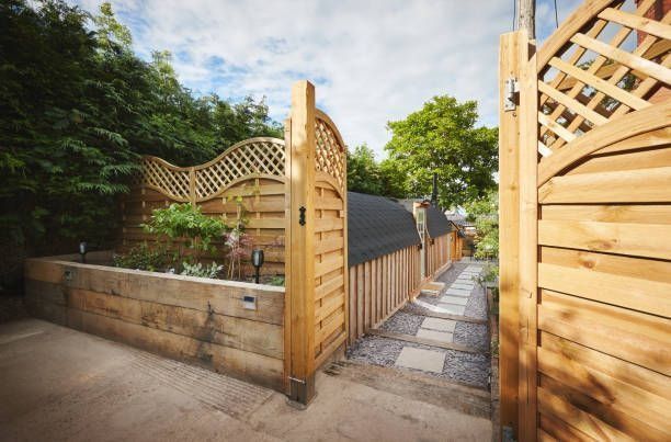 Wooden fence and gate leading to a pathway lined with a low wall and plants.