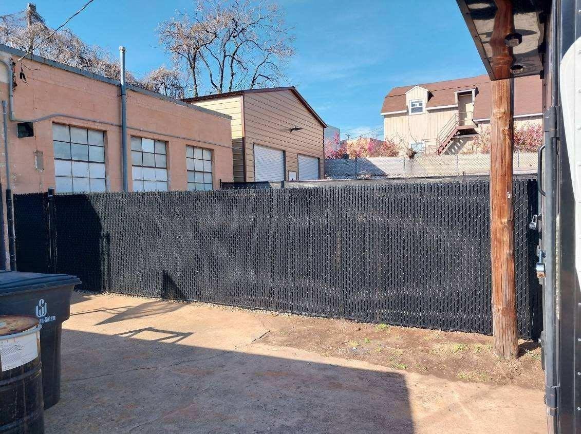 Black fence in alley with buildings and blue sky.