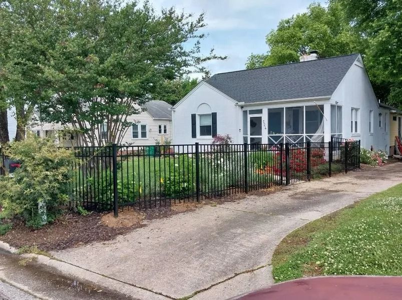 A small, white house with a screened porch behind a black metal fence on a driveway.