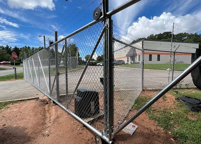 Chain-link fence with a gate, outdoor setting with a building and sky in the background.