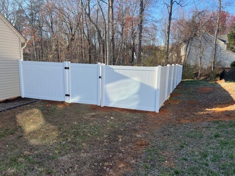 White vinyl fence with gate in a yard with trees.