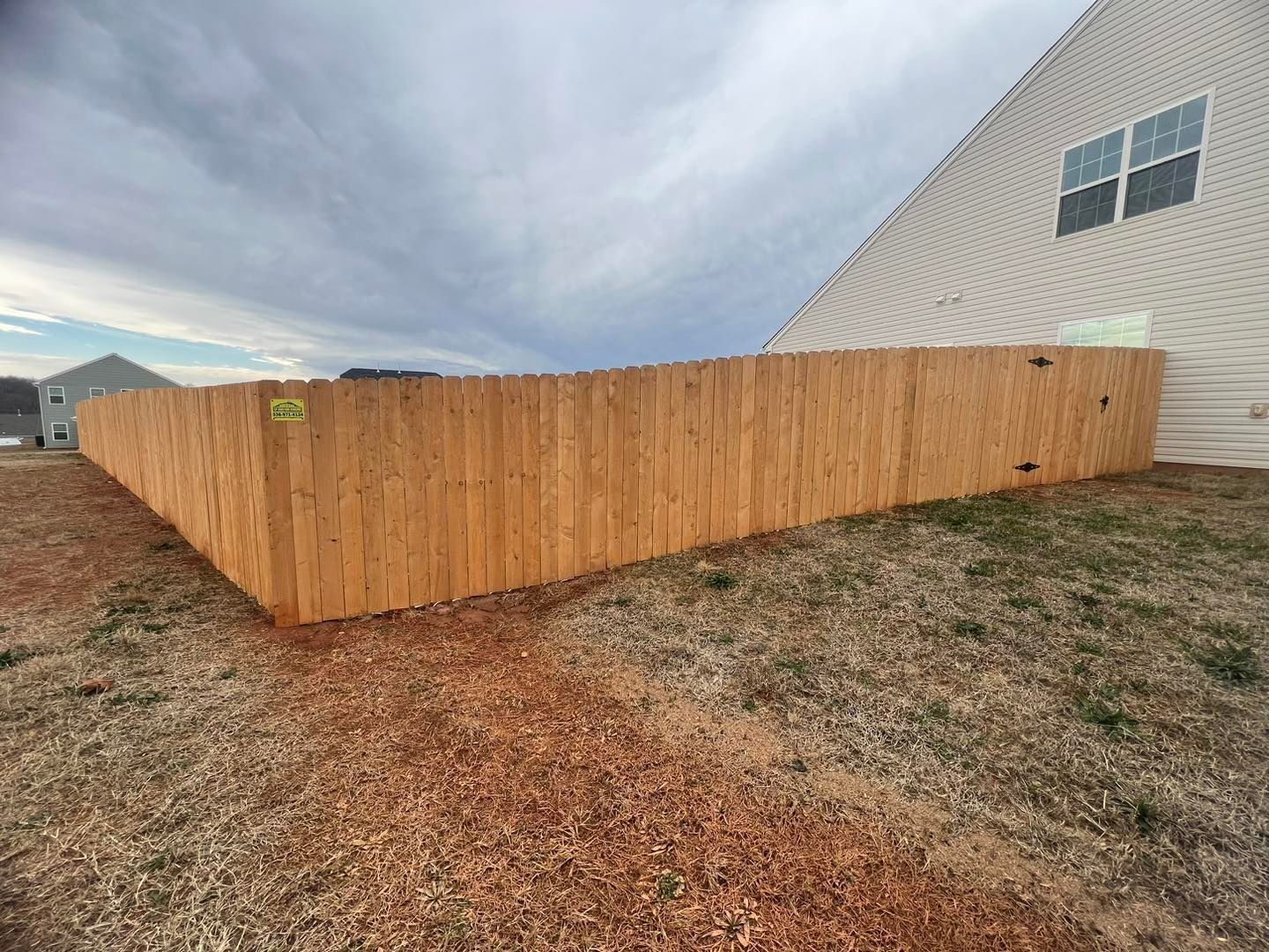 Wooden fence surrounding a yard, next to a beige house, under a cloudy sky.
