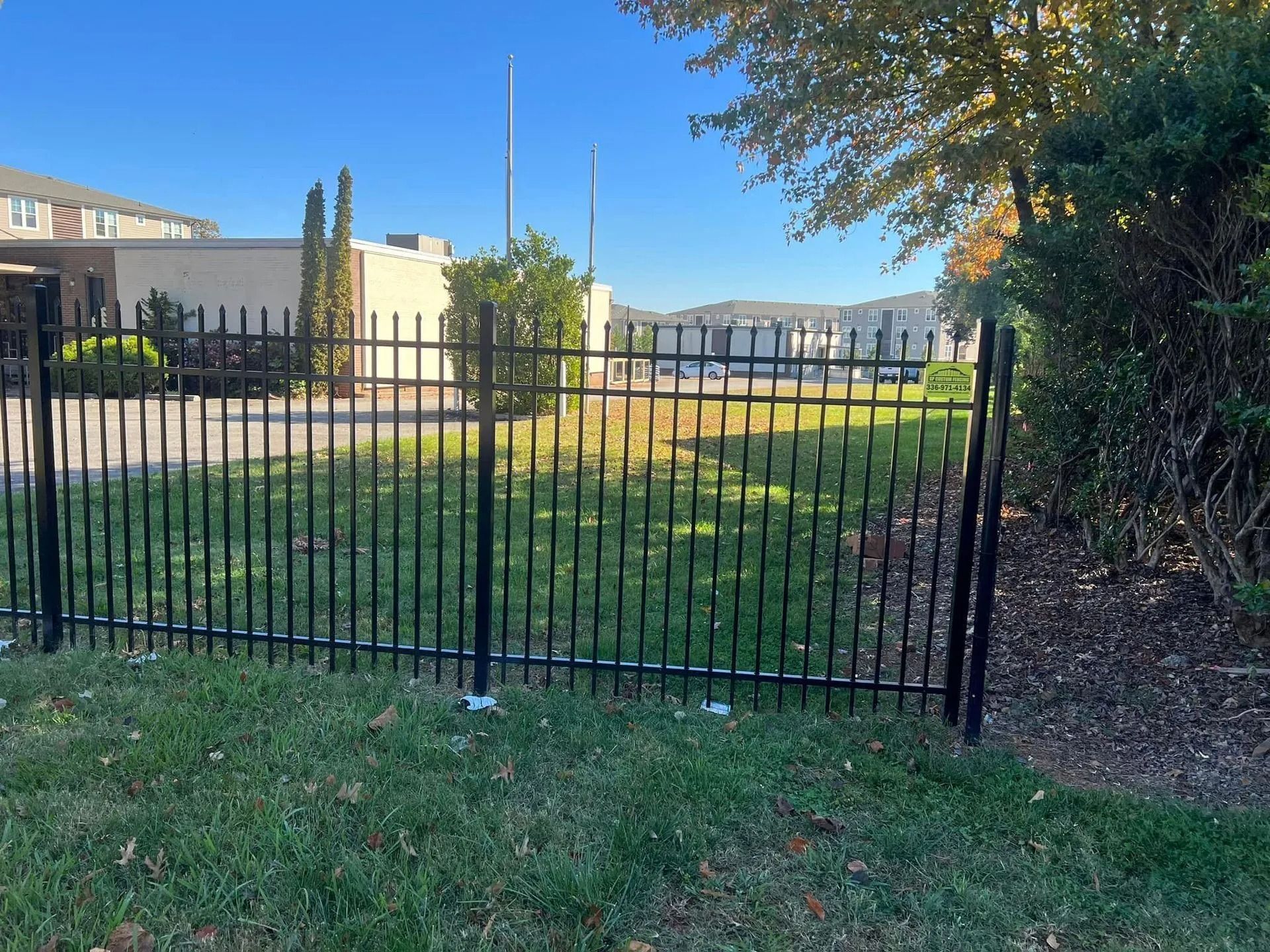 Black metal fence in front of a building and some trees.